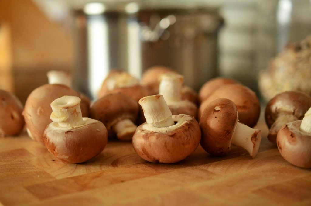 Fresh cremini mushrooms with trimmed stems arranged on a wooden butcher block cutting board